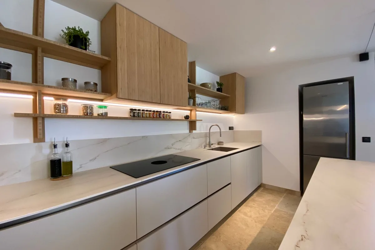 Handleless fitted kitchen with oak shelving and a stone worktop