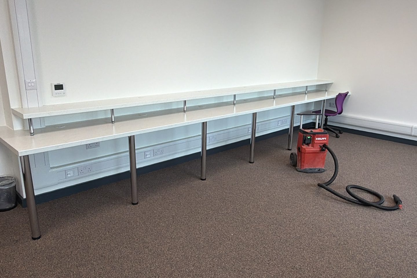 Twin-tier bench run fixed along a wall, upper tier on chrome legs above a lower worktop